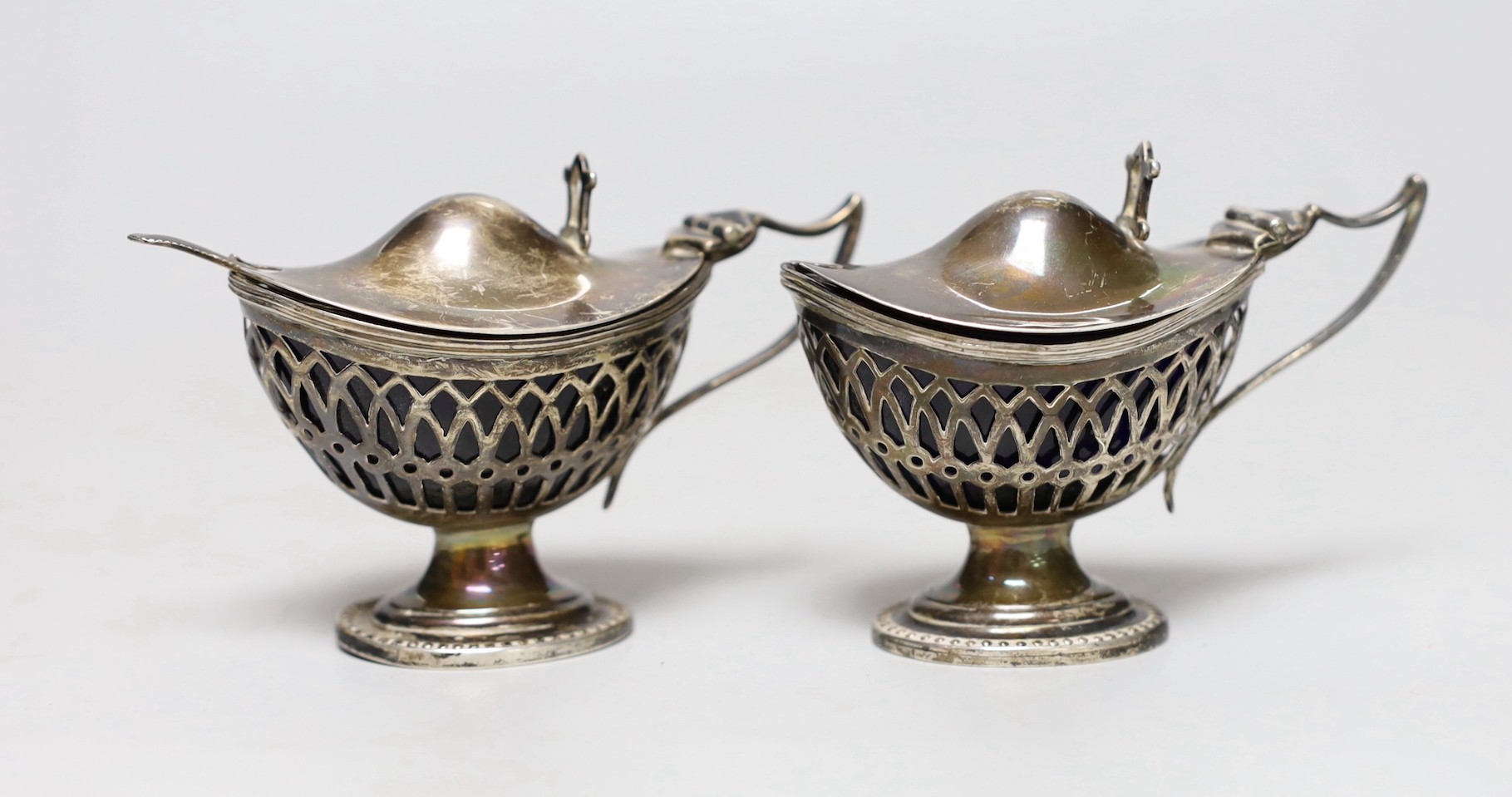 A pair of Edwardian pieced silver pedestal boat shaped mustard pots, E.S. Barnsley & Co, Birmingham, 1903, length 91mm, one with associated silver condiment spoon.